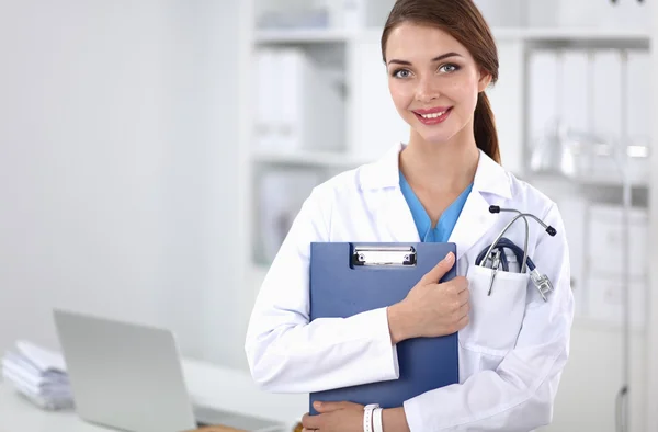 Médecin souriante avec un dossier en uniforme debout à l'hôpital — Photo