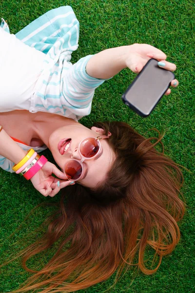 Mooie jonge vrouw selfie maken door haar telefoon liggend in groene gras — Stockfoto