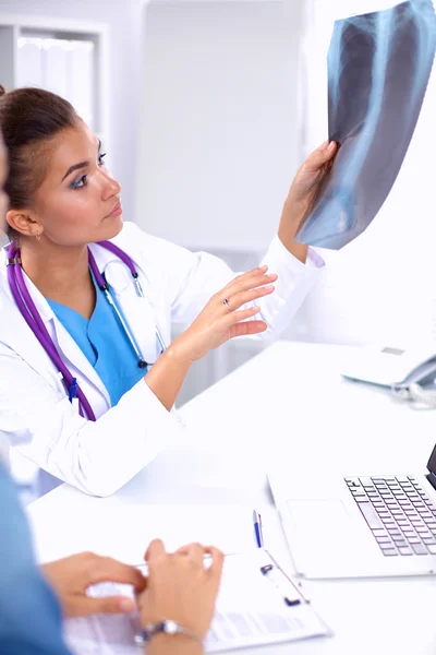 Jonge vrouwelijke arts studeert röntgenfoto zittend op het bureau — Stockfoto