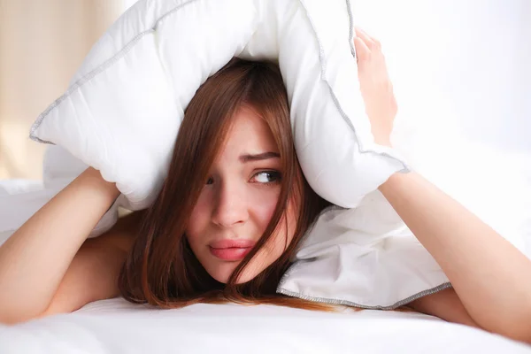 Mujer acostada en la cama y cerrando las orejas con almohada —  Fotos de Stock