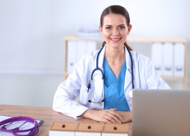 Güzel, genç, gülümseyen bayan doktor masada oturuyor ve yazıyor..