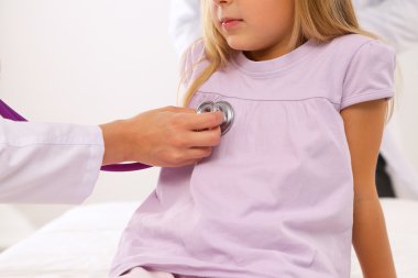 Kadın doktor ameliyatta steteskopla çocuğu muayene ediyor.