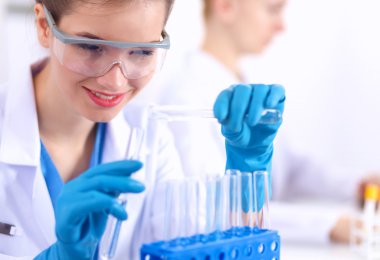 Kadın araştırmacı, beyaz arka planda izole edilmiş ilaç şişeleri ve mataralarla çevrili.