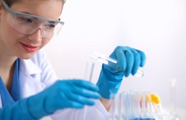 Kadın araştırmacı, beyaz arka planda izole edilmiş ilaç şişeleri ve mataralarla çevrili.