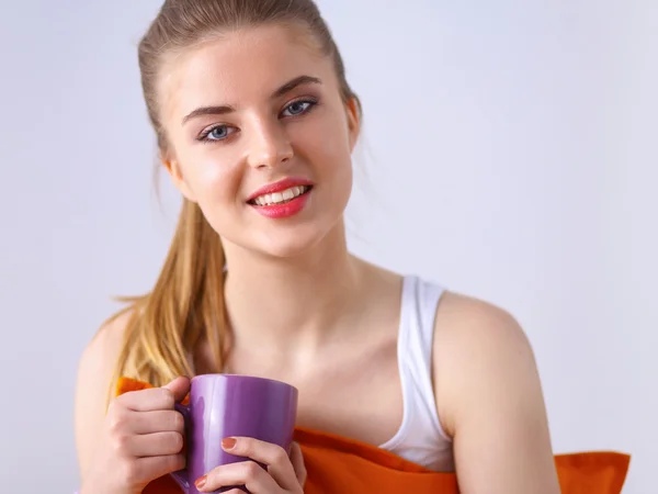 Young woman sitting with pillow and holding a cup of tea — Stock Photo, Image
