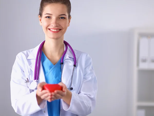 Young woman doctor holding a red heart, standing in hospital — Stock Photo, Image