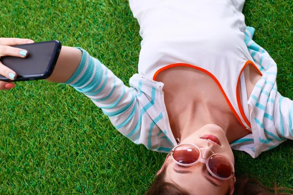 Bela jovem mulher fazendo selfie por seu telefone enquanto deitado na grama verde — Fotografia de Stock