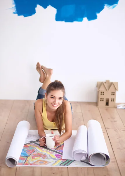 Jonge vrouw op de vloer liggen en kijken naar blauwdruk van nieuwe huis — Stockfoto