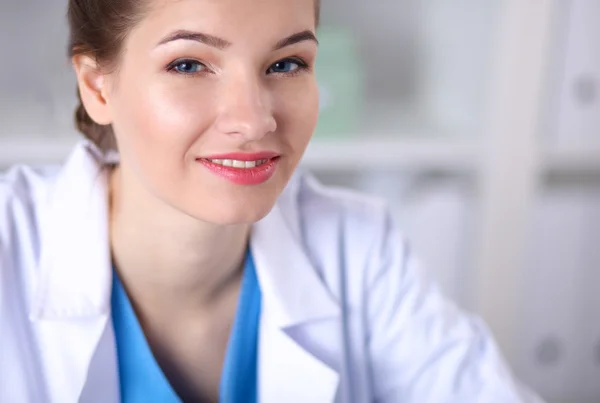 Bonito jovem sorridente médico feminino sentado na mesa . — Fotografia de Stock