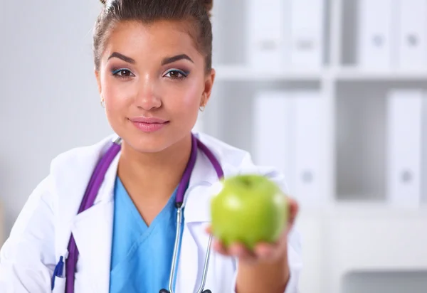 Kvinnlig läkare hand håller ett grönt äpple, sitter vid skrivbordet — Stockfoto