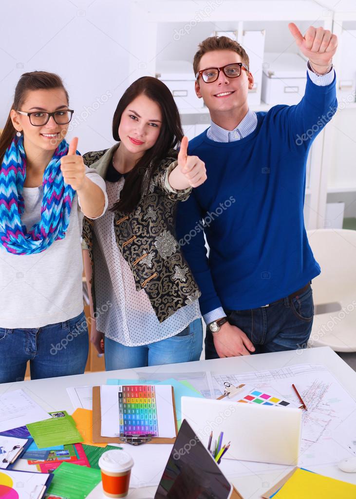 Young business people standing at office near desk and showing ok