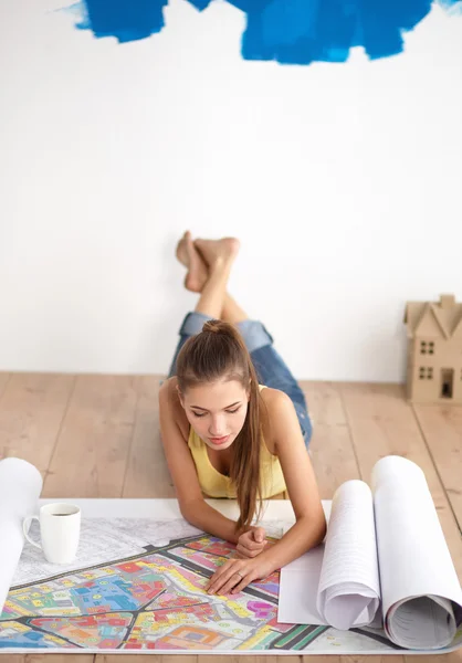 Mujer joven acostada en el suelo y mirando el plano de la nueva casa —  Fotos de Stock