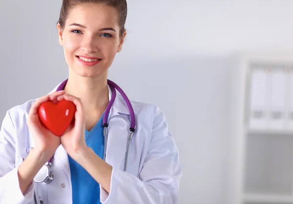 Young woman doctor holding a red heart, standing — Stock Photo, Image