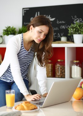 Dizüstü bilgisayar kullanarak ve mutfakta oturmuş çekici genç kadın 