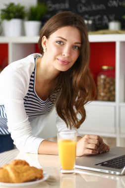 Dizüstü bilgisayar kullanarak ve mutfakta oturmuş çekici genç kadın 