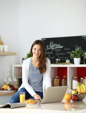 Dizüstü bilgisayar kullanarak ve mutfakta oturmuş çekici genç kadın 