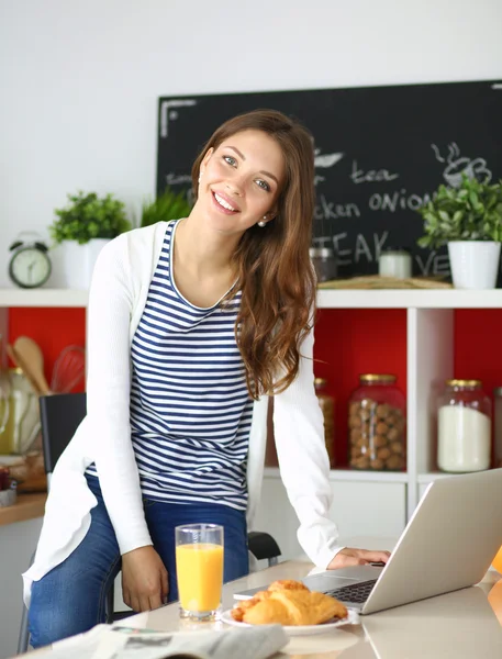 Attraktiv ung kvinna med laptop och sitter i köket — Stockfoto