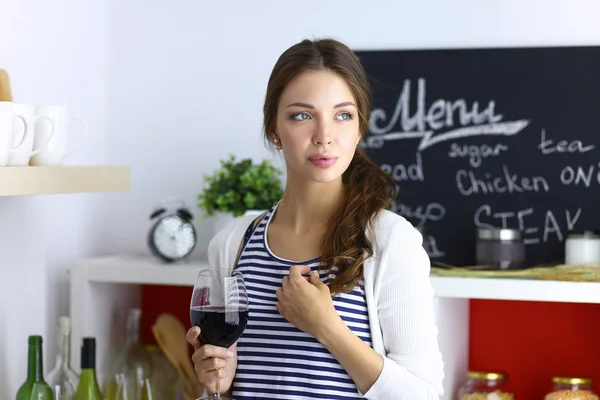 Mujer bonita bebiendo un poco de vino en casa en la cocina —  Fotos de Stock