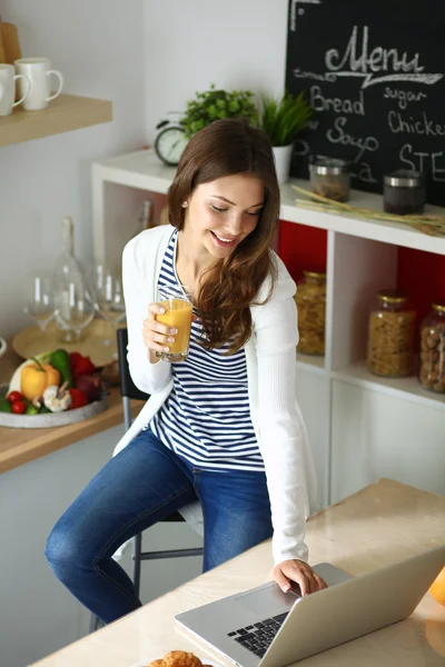 Aantrekkelijke jonge vrouw met behulp van laptop en zitten in de keuken — Stockfoto