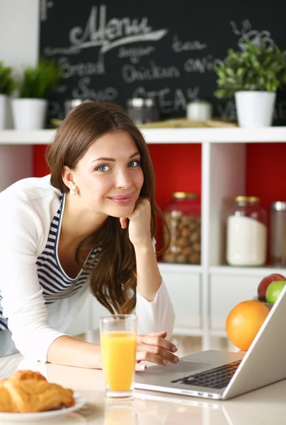 Mujer joven atractiva usando el ordenador portátil y sentado en la cocina —  Fotos de Stock