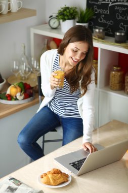 Dizüstü bilgisayar kullanarak ve mutfakta oturmuş çekici genç kadın 