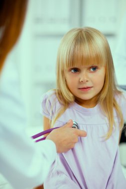 Kadın doktor ameliyatta steteskopla çocuğu muayene ediyor.