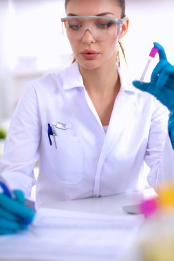 Kadın araştırmacı, beyaz arka planda izole edilmiş ilaç şişeleri ve mataralarla çevrili.