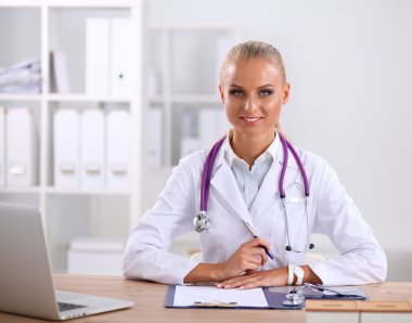 Güzel, genç, gülümseyen bayan doktor masada oturuyor ve yazıyor..