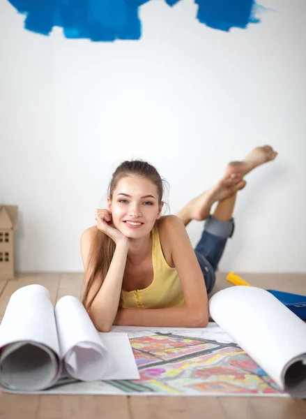 Young woman lying on the floor and looking at blueprint of new house — Stock Photo, Image