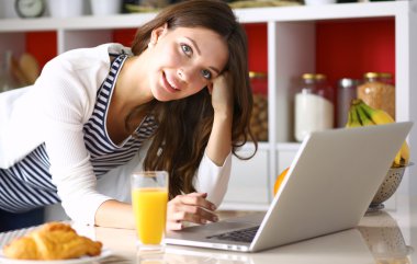 Dizüstü bilgisayar kullanarak ve mutfakta oturmuş çekici genç kadın 