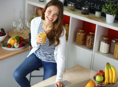 Dizüstü bilgisayar kullanarak ve mutfakta oturmuş çekici genç kadın 