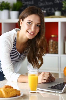 Dizüstü bilgisayar kullanarak ve mutfakta oturmuş çekici genç kadın 