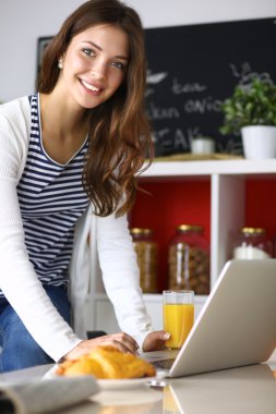 Dizüstü bilgisayar kullanarak ve mutfakta oturmuş çekici genç kadın 