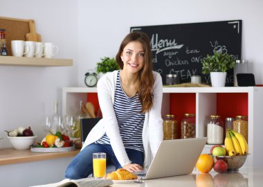 Dizüstü bilgisayar kullanarak ve mutfakta oturmuş çekici genç kadın 