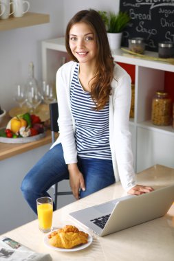 Dizüstü bilgisayar kullanarak ve mutfakta oturmuş çekici genç kadın 