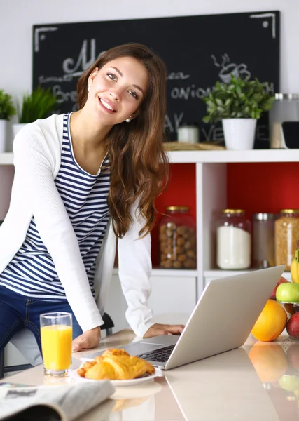 Attraktiv ung kvinna med laptop och sitter i köket — Stockfoto