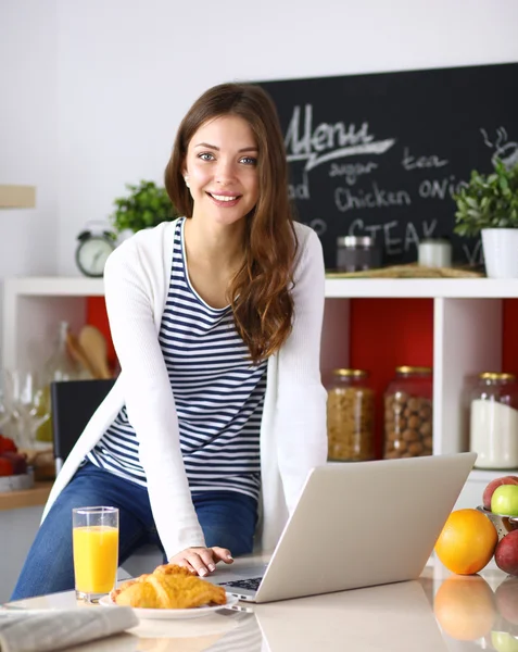 Attraktive junge Frau mit Laptop und sitzt in der Küche — Stockfoto