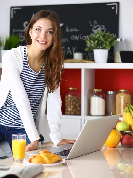 Attraktiv ung kvinna med laptop och sitter i köket — Stockfoto