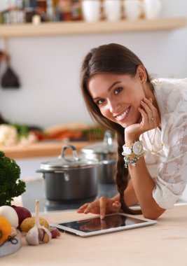 Mutfakta yemek yapmak için tablet bilgisayar kullanan genç bir kadın.