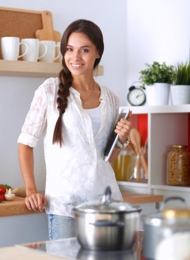 Mutfakta yemek yapmak için tablet bilgisayar kullanan genç bir kadın.