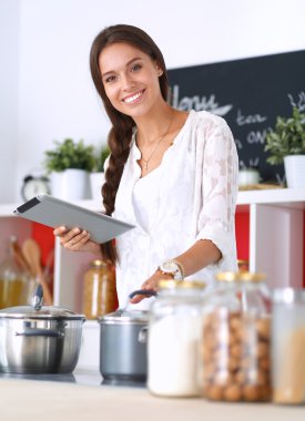 Mutfakta yemek yapmak için tablet bilgisayar kullanan genç bir kadın.