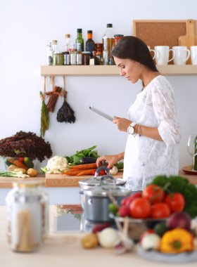 Mutfakta yemek yapmak için tablet bilgisayar kullanan genç bir kadın.