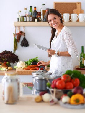 Mutfakta yemek yapmak için tablet bilgisayar kullanan genç bir kadın.
