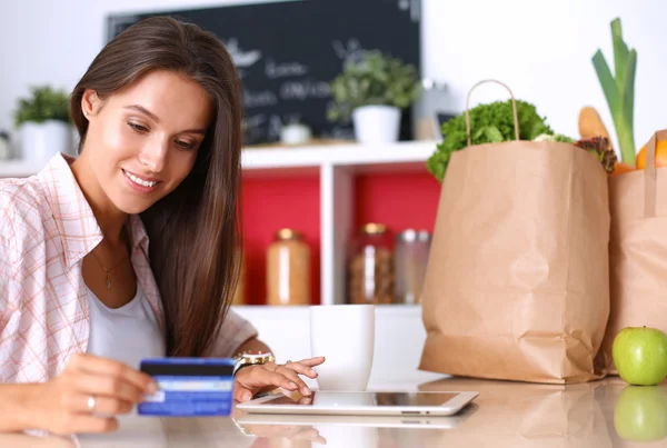 Femme souriante achats en ligne en utilisant tablette et carte de crédit dans la cuisine — Photo