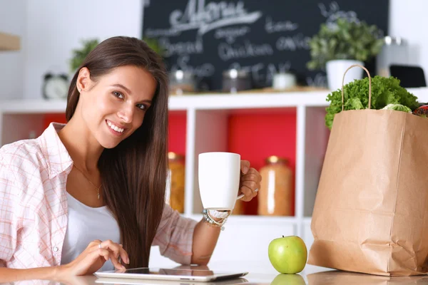 Mujer usando una tableta mientras bebe té en su cocina — Foto de Stock