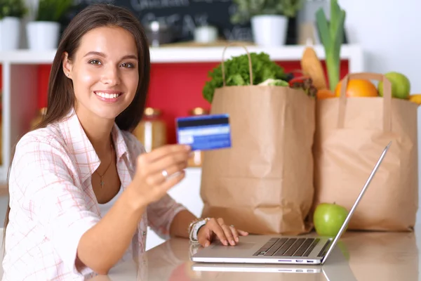 Mulher sorrindo compras on-line usando tablet e cartão de crédito na cozinha — Fotografia de Stock