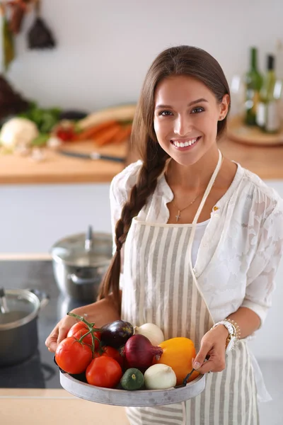 Usmívající se mladá žena drží zeleninu stojící v kuchyni — Stock fotografie