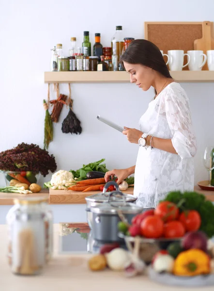 Young woman using a tablet computer to cook in her kitchen — Stock Photo, Image