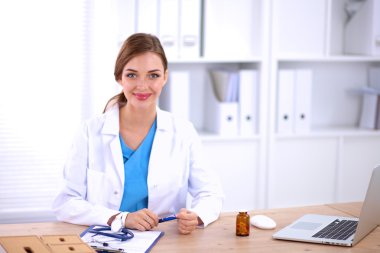 Güzel, genç, gülümseyen bayan doktor masada oturuyor ve yazıyor..