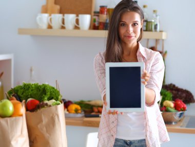 Mutfakta yemek yapmak için tablet bilgisayar kullanan genç bir kadın.